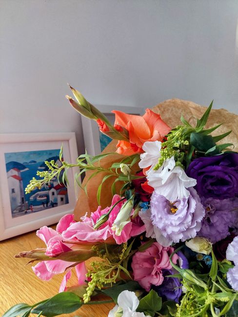 A close-up of a fresh floral bouquet featuring an assortment of flowers including pink and purple eustomas, white lisianthus, and orange snapdragons, arranged with greenery and placed on a wooden surf