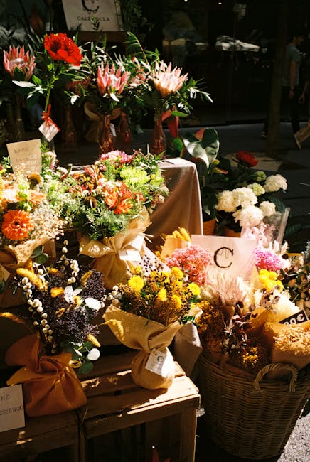 A display of freshly arranged floral bouquets and arrangements at a flower shop, featuring a variety of flowers including red roses, pink lilies, orange gerbera daisies, yellow chrysanthemums, and bab